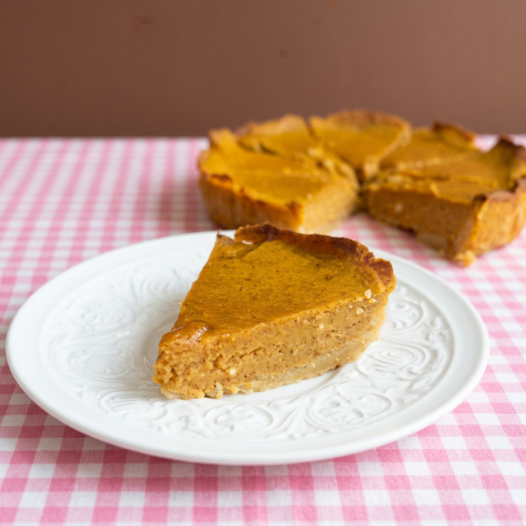 Polished pumpkin pie slice and whole pie with cocoa-brown background and pink gingham
